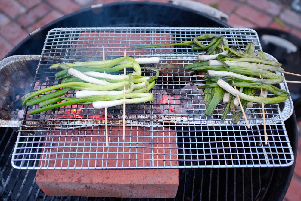 Scallions cooking over very hot coals (on the left) and being kept warm over older coals (on the right)